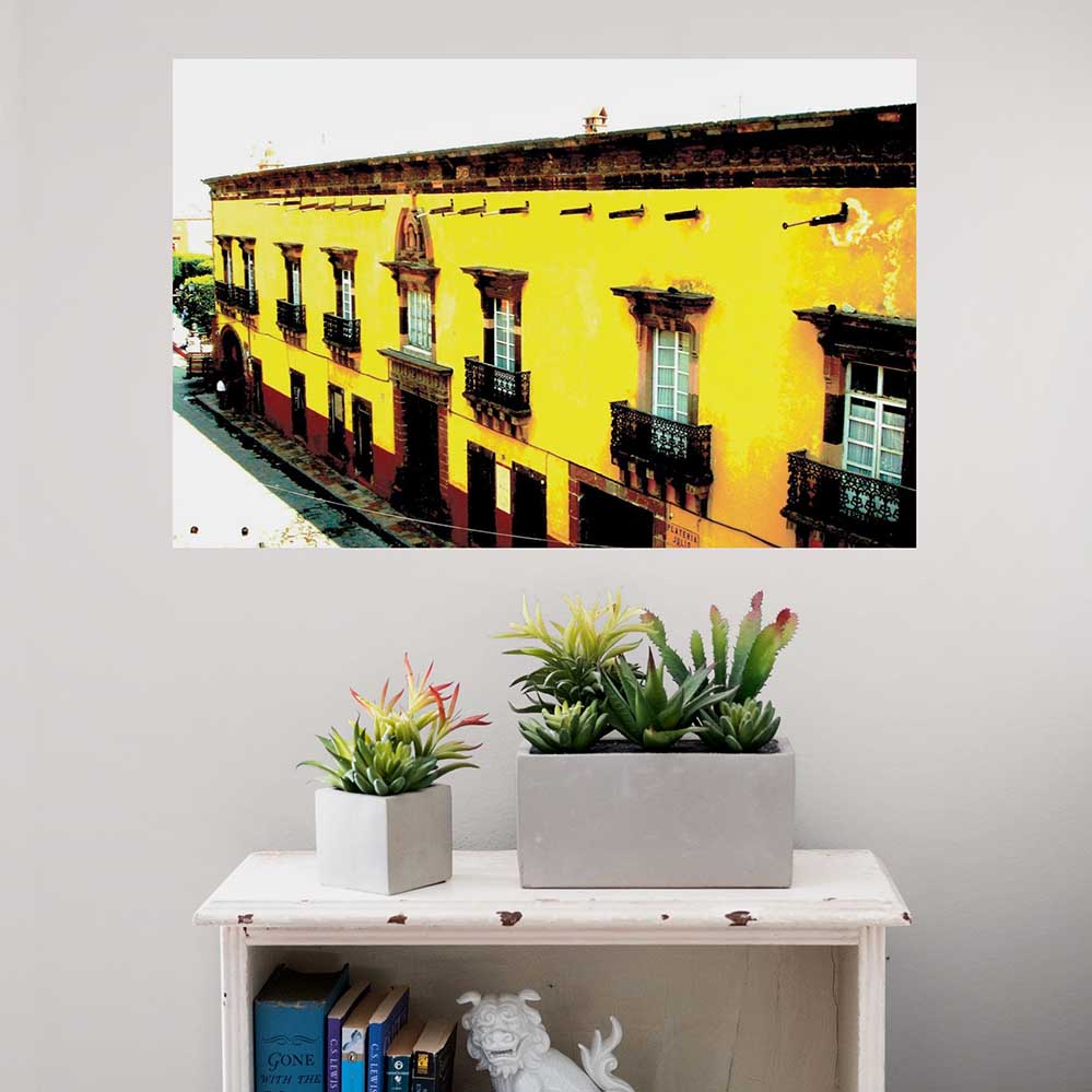 24 inch yellow Mexican hotel with balconies displayed on a wall above a bookcase with planters