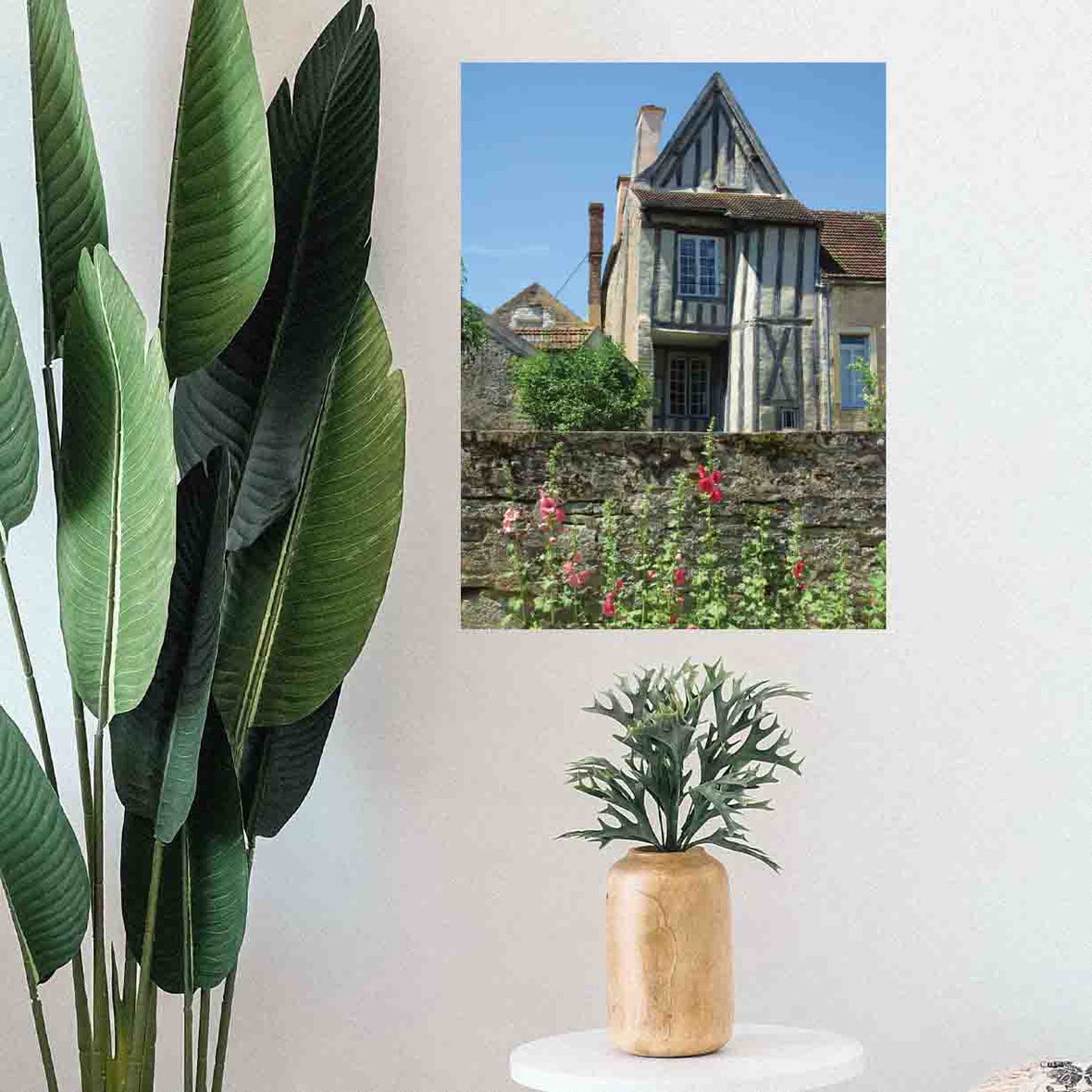 24 inch poster of a traditional half timbered house in Noyers France with flowers in foreground displayed on wall above a stooled plant