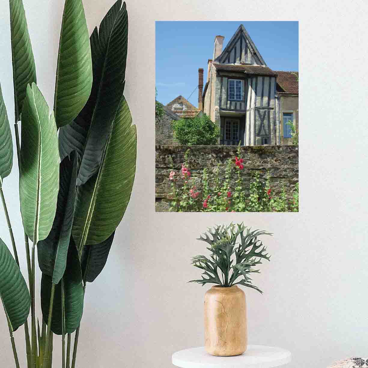 24 inch decal of a half timbered house with a wall and flowers in foreground installed on a wall above a plant on stool