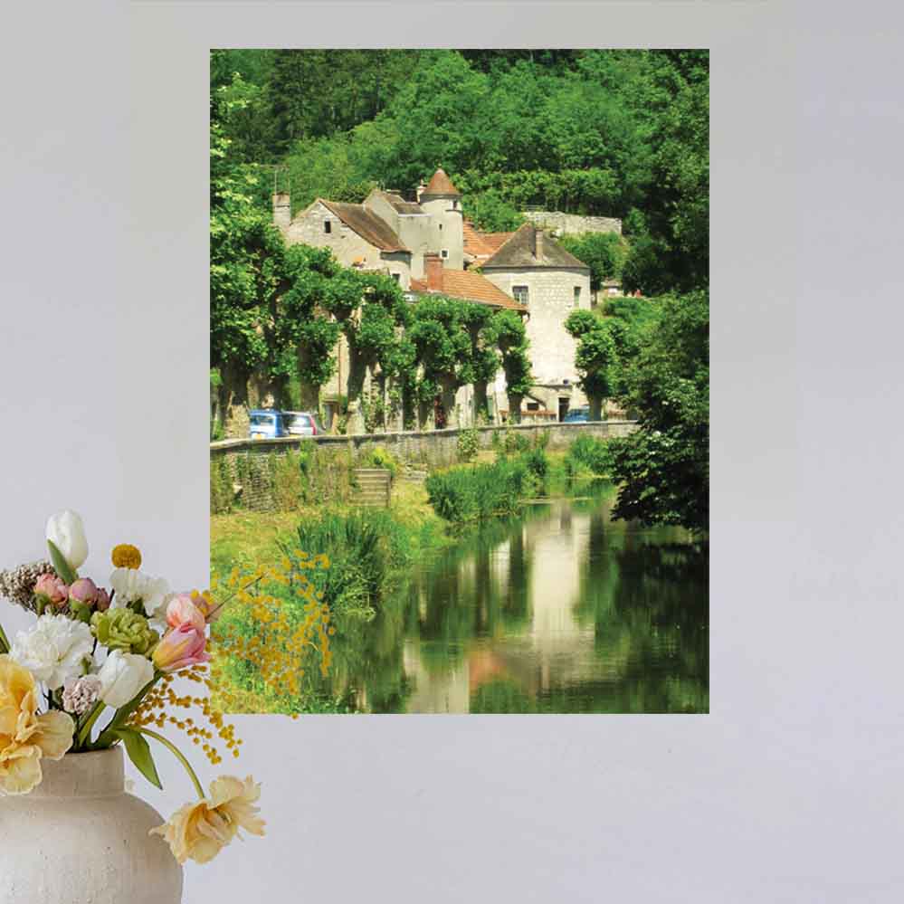 24 inch poster of a old stone building in France along a river displayed on wall above a vase with flowers