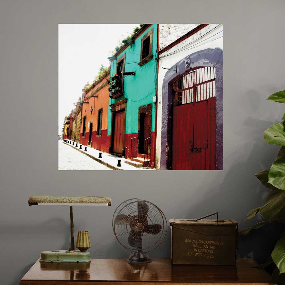 36 inch colorful Mexican street scene with buildings poster displayed on a gray wall above a wooden table