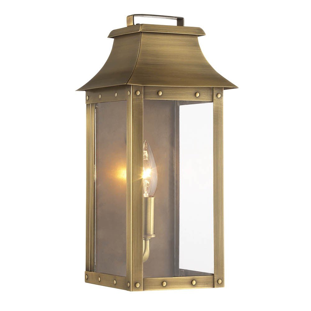 Front left angle view of the lighted Manchester 1-Bulb Aged Brass Pocket Wall Light with clear glass and solid brass frame – outdoor lantern style wall sconce