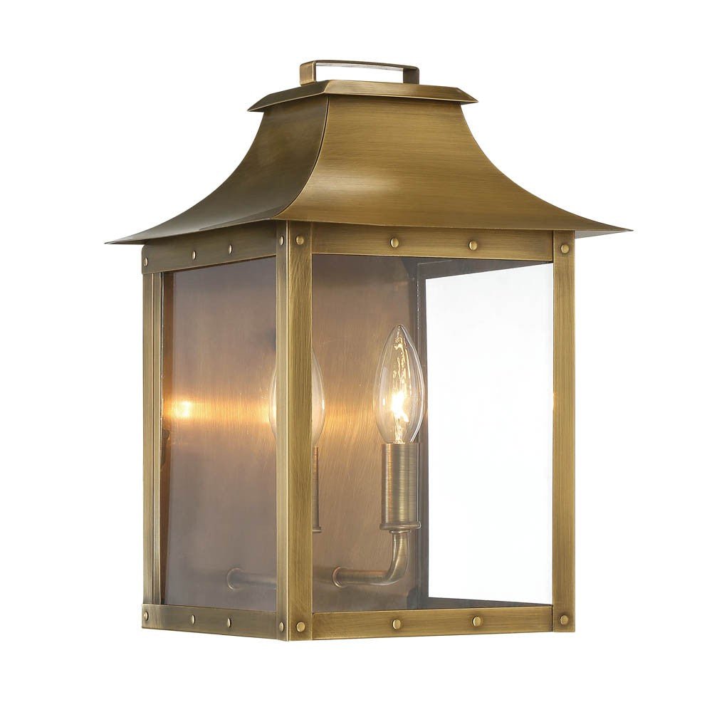 Front left angle view of the lighted Manchester 2-Bulb Aged Brass Pocket Wall Lantern with Clear Glass – Outdoor Rustic Brass Lighting Fixture