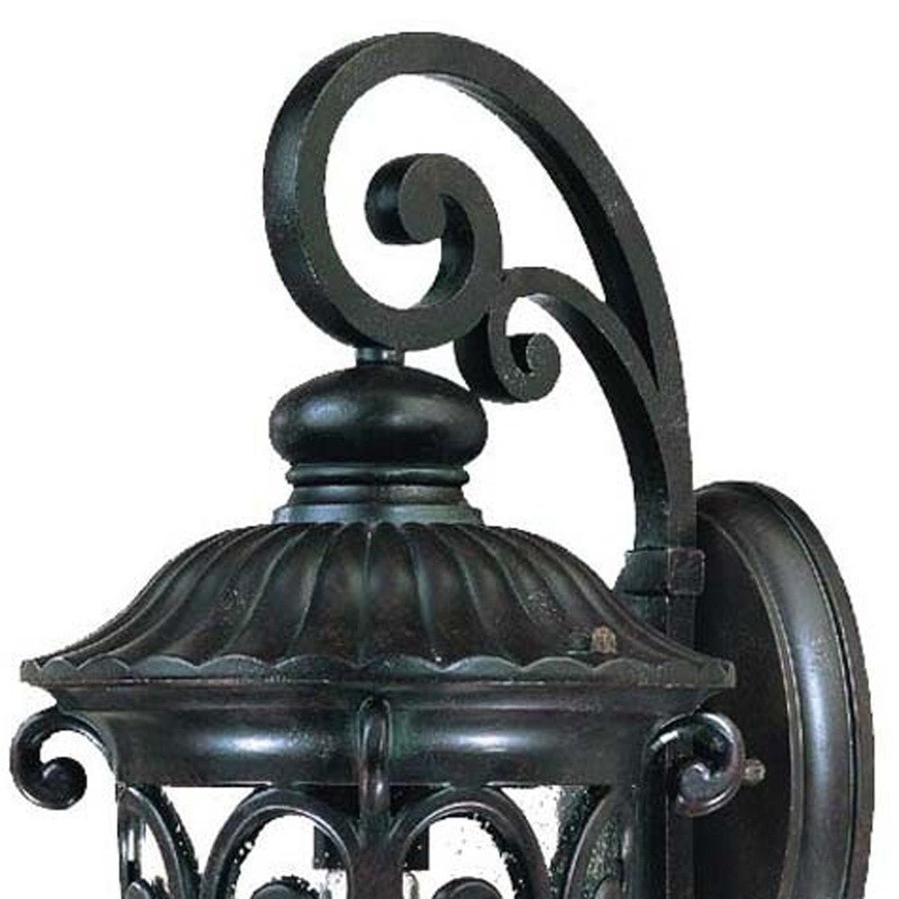 Zoomed in view of the wall plate, scroll arm and lantern top of the Naples marbleized black outdoor wall light with ornate scrollwork and seeded glass panels