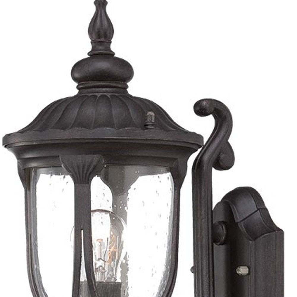 Zoomed in view of the wall plate, arm, and fixture top of the lighted Black cast aluminum outdoor glass lantern wall light with curved shield silhouette