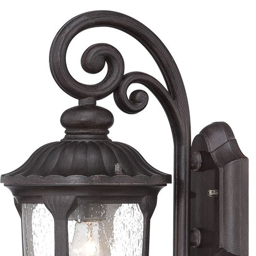 Zoomed in view of the wall plate, scroll arm and lantern top of the lighted Black cast aluminum outdoor glass lantern wall sconce with clear panels