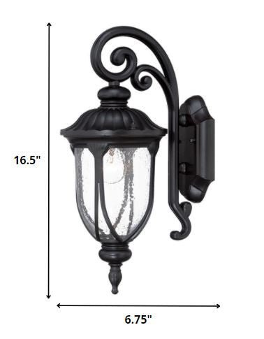 Matte black cast aluminum outdoor glass lantern wall sconce with clear panels shown with dimensions of 16 point 5 inches high by 6 point 75 inches wide