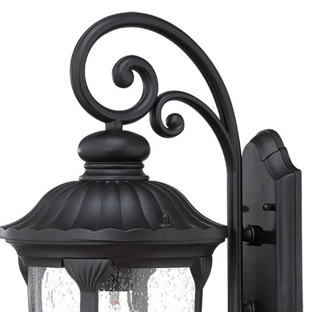 Zoomed in view of the wall plate, scroll arm and top of fixture of the XL matte black cast aluminum outdoor hanging lantern wall sconce with clear glass panels