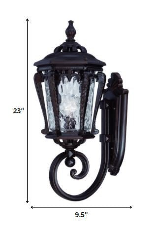 Architectural bronze outdoor wall light with hammered glass and scroll detailing shown with dimensions of 23 inches high by 9 point 5 inches wide