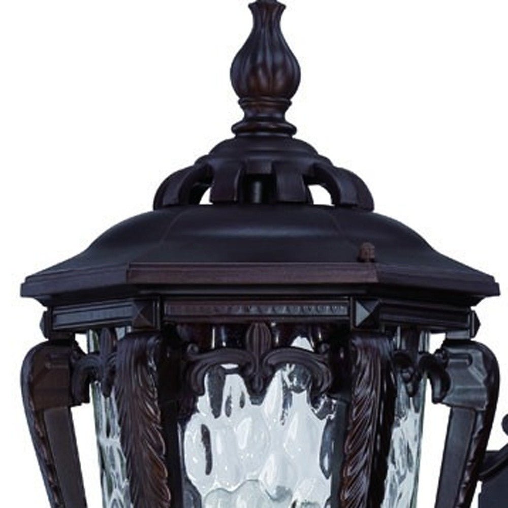 Zoomed in view of the elaborate fixture top and glass shade of the Architectural bronze outdoor wall light with hammered glass and scroll detailing