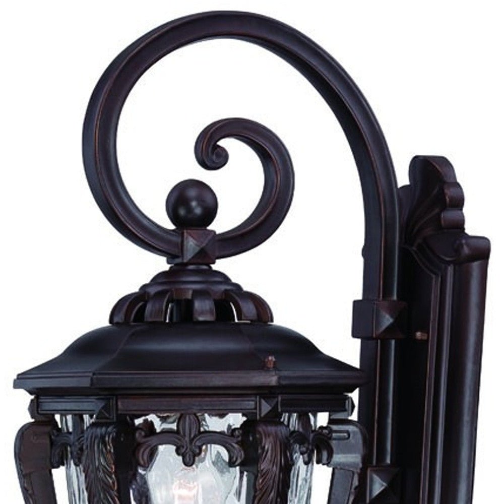 Zoomed in view of the scroll arm and fixture top of the lighted Architectural bronze hanging outdoor wall light with hammered glass shade
