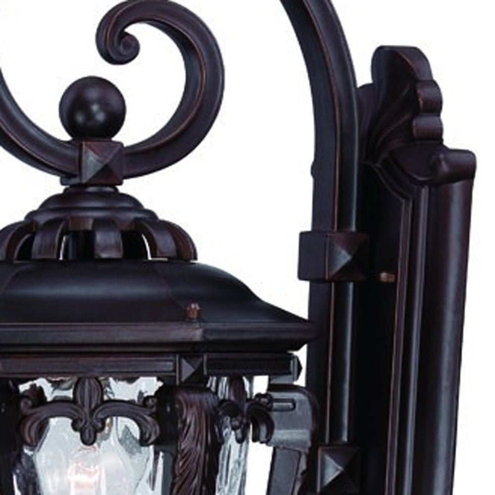 Zoomed in view of the wall plate, arm and partial fixture of the lighted Architectural bronze hanging outdoor wall light with hammered glass shade