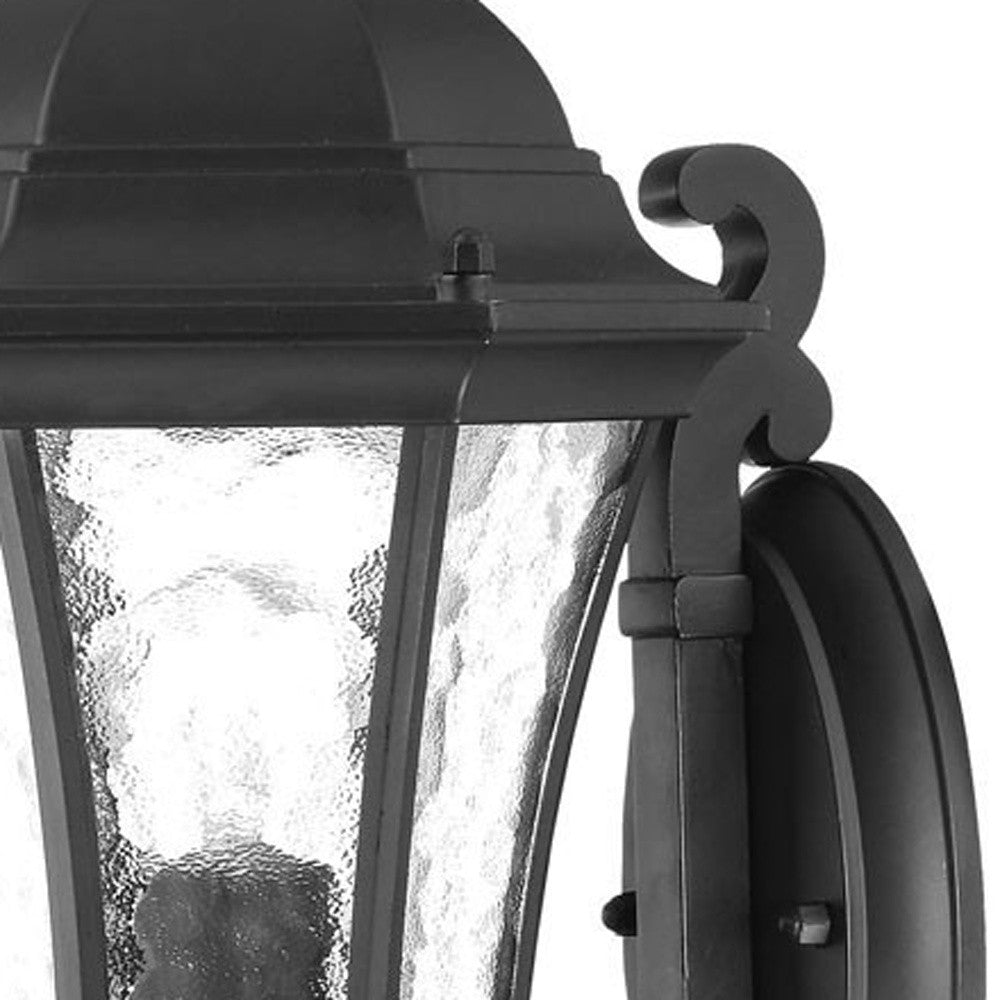 Zoomed in view of the arm, fixture top, wall plate, and shade of the Matte black tapered outdoor lantern wall light with hammered glass panels