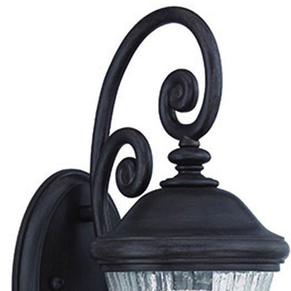 Zoomed in view of the scroll arms and fixture top of the lighted Matte Black urn shaped outdoor wall light with raindrop glass globe mounted on wall