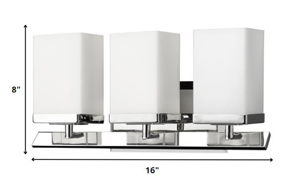 Three-light silver wall sconce with frosted glass shades and modern beveled metal base shown with dimensions of eight inches high by sixteen inches wide