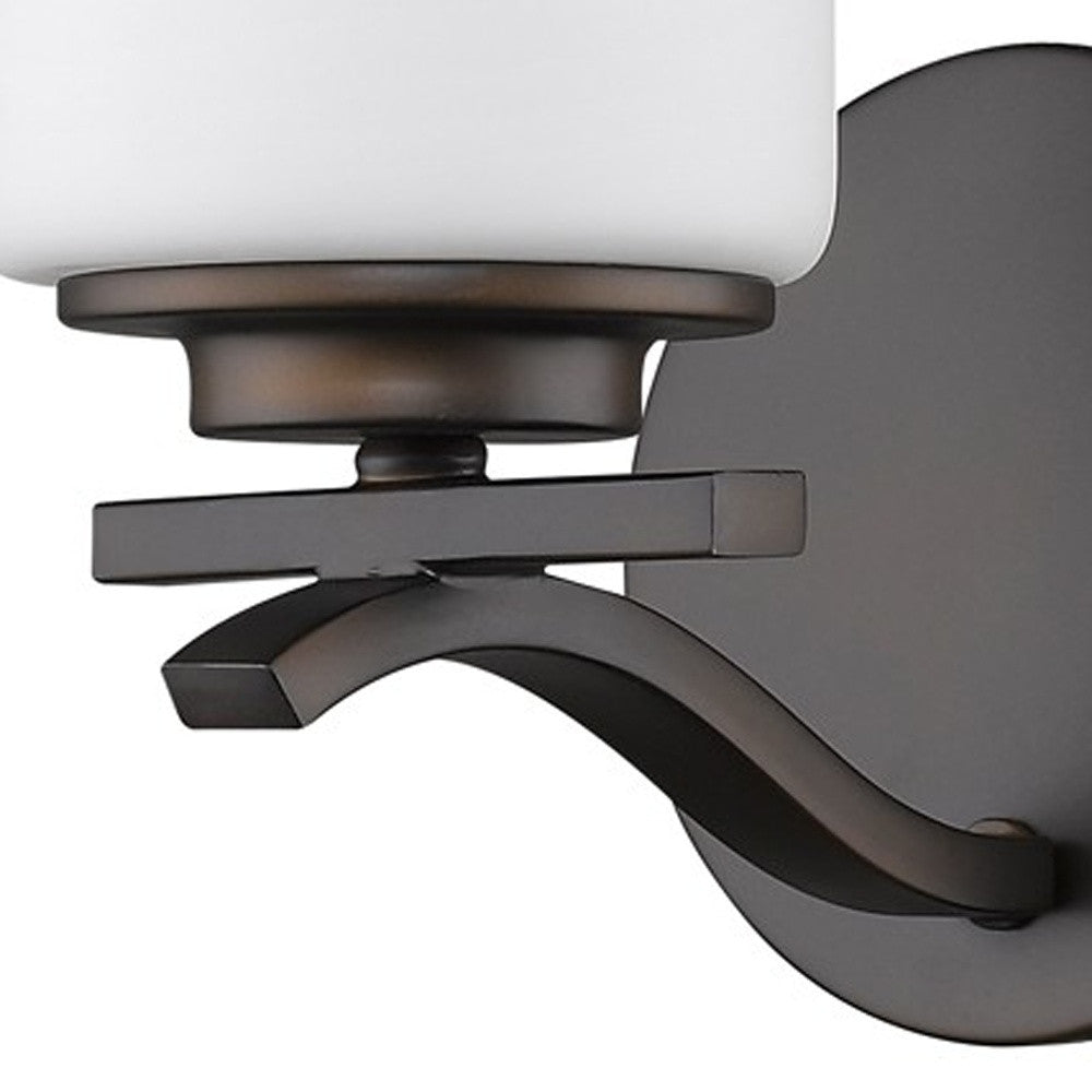 Zoomed in view of the wall plate, arm and shade base of the  One-light bronze wall sconce with frosted cylindrical glass shade and curved metal arm