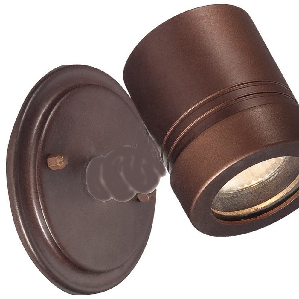 Close-up view of a lighted Adjustable bronze outdoor wall spotlight with round backplate and modern cylindrical head