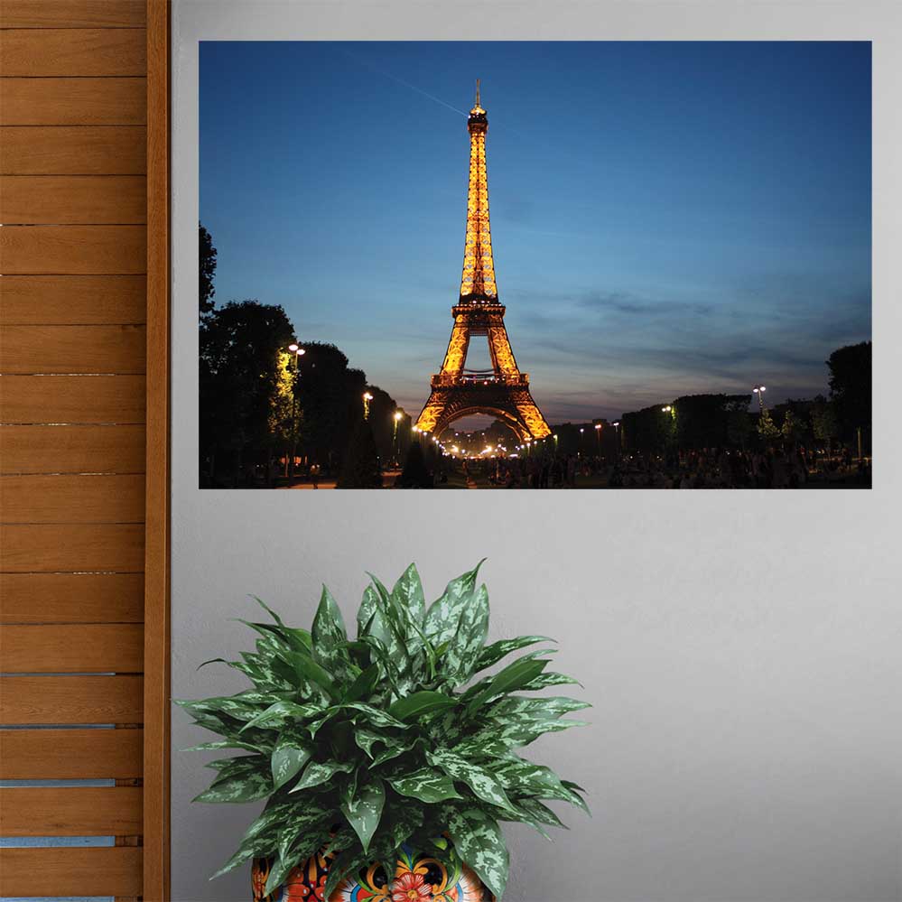 48 inch poster of the Eiffel Tower illuminated at dusk displayed on a wall above a large vase with plant on floor