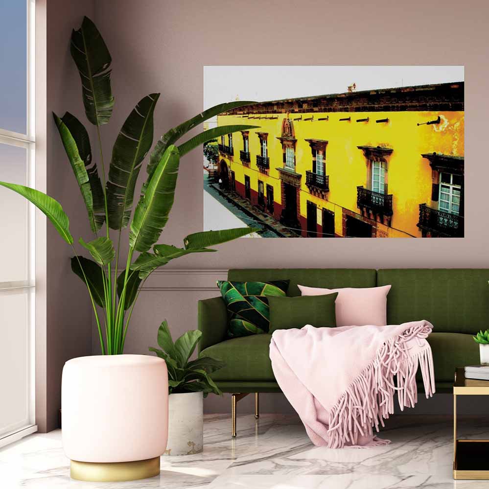 60 inch yellow Mexican hotel with balconies displayed on a wall above a green sofa with pink blanket
