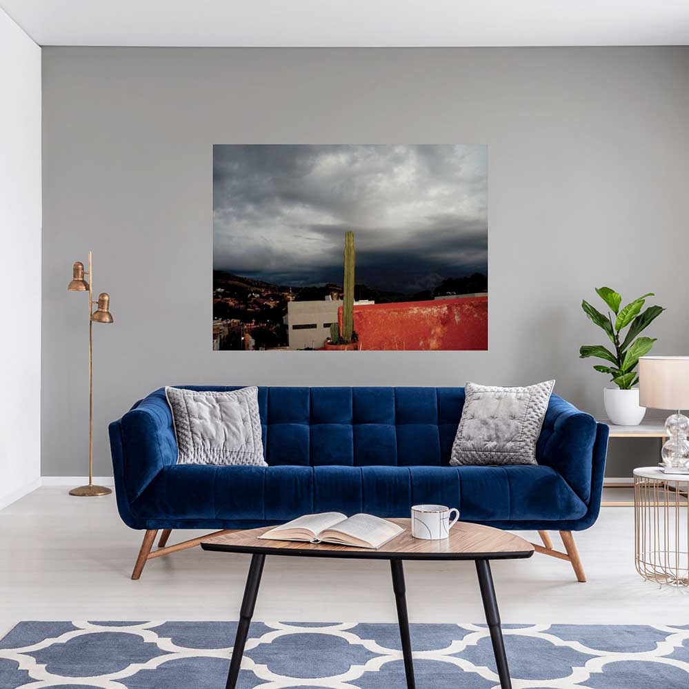 60 inch poster of a dark cloudy storm brewing in Mexico with a potted cactus in foreground displayed above a blue sofa