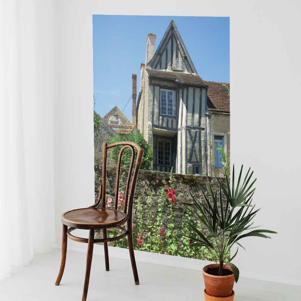 60 inch poster of a traditional half timbered house in Noyers France with flowers in foreground displayed on wall with a chair and potted plant in front of it