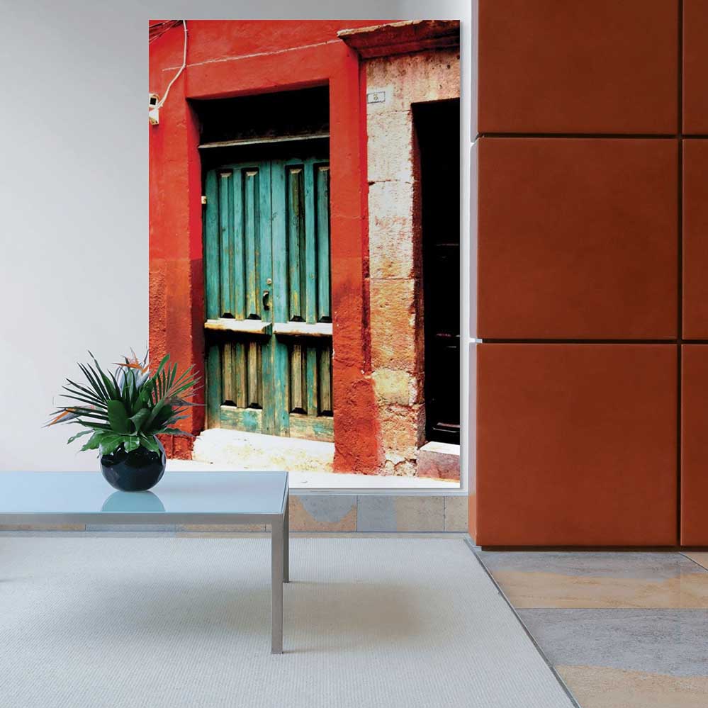 72 inch poster of a red framed green door of a Mexican home displayed on a wall with coffee table and potted plant in foreground