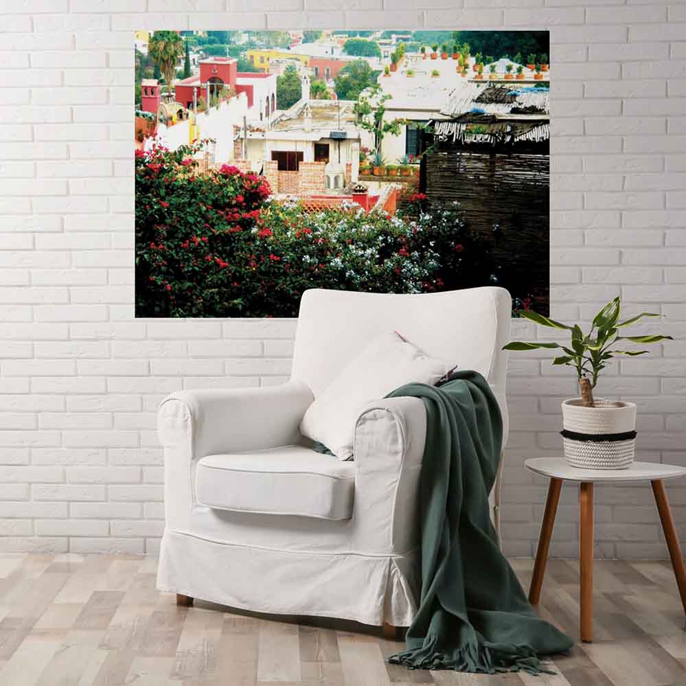 72 inch poster of a rooftop garden on Mexican home looking down over town displayed on wall with a linen chair and stool with plant in the foreground