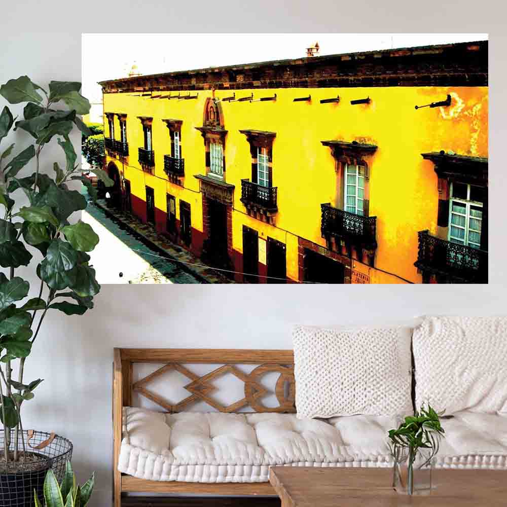 72 inch yellow Mexican hotel with balconies displayed on a wall above a wooden bench with cushions