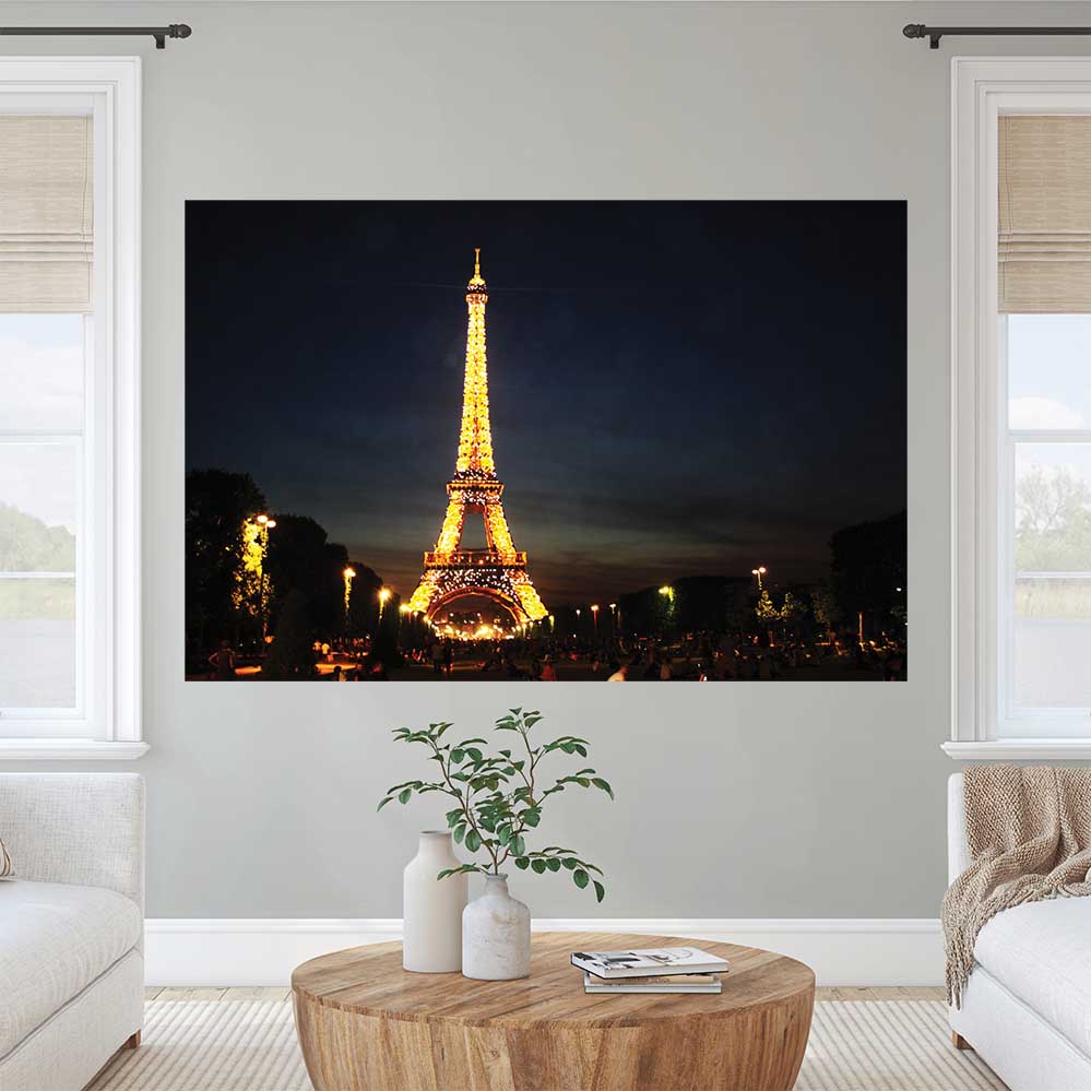 72 inch poster of the illuminated Eiffel Tower at nigh against a dark sky displayed on a wall between two windows in a living room
