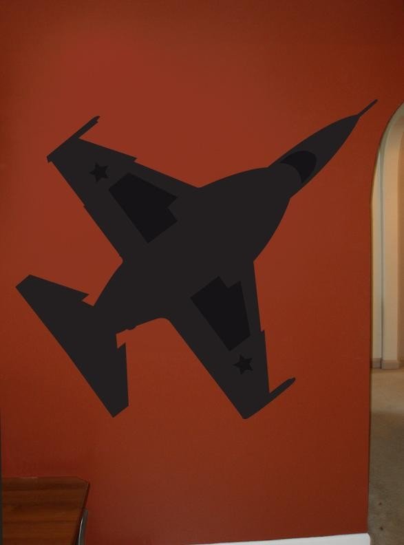 A black vinyl wall decal of a fighter jet mounted on a terracotta orange wall, with a glimpse of a doorway on the right and a wooden surface at the bottom left.