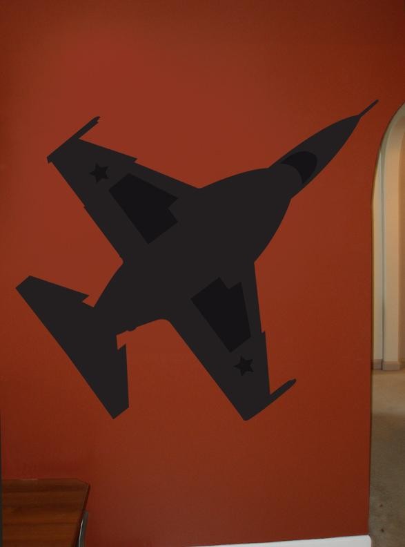 A black vinyl wall decal of a fighter jet mounted on a terracotta orange wall, with a glimpse of a doorway on the right and a wooden surface at the bottom left.