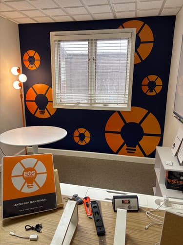 Company logo black and orange wall mural installed on wall with window.